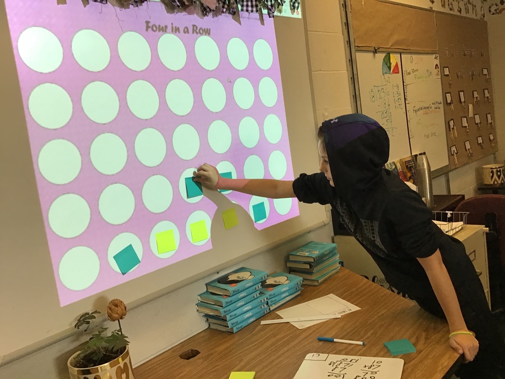 Student Placing sticky note on board during playing a game of Connect Four